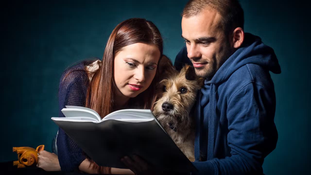Un couple lisant un livre avec leur chien entre eux, tous trois concentrés.