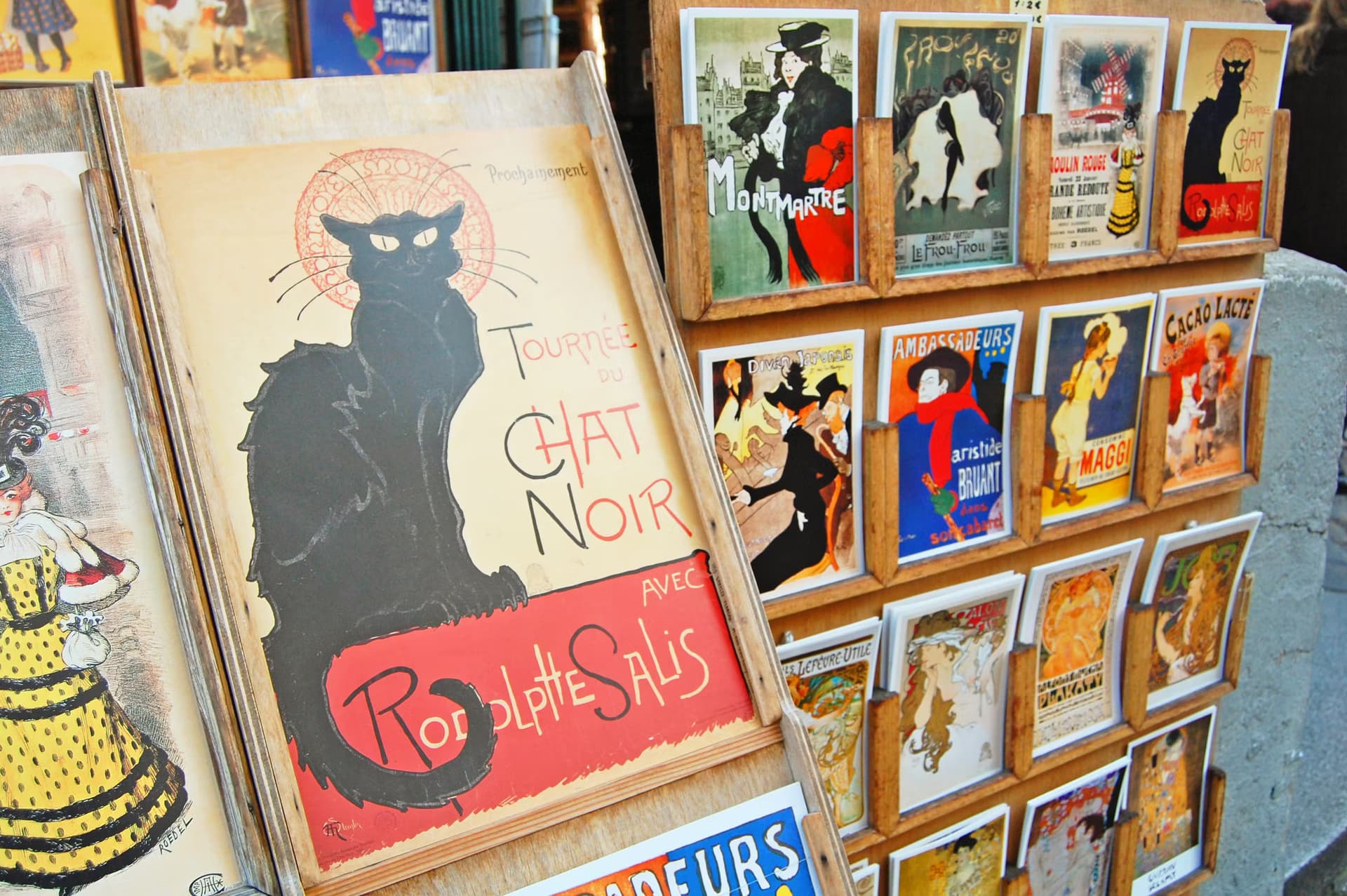 Affiches rétro de Montmartre, dont l'emblématique affiche 'Tournée du Chat Noir' de Rodolphe Salis, exposées dans un présentoir à Paris